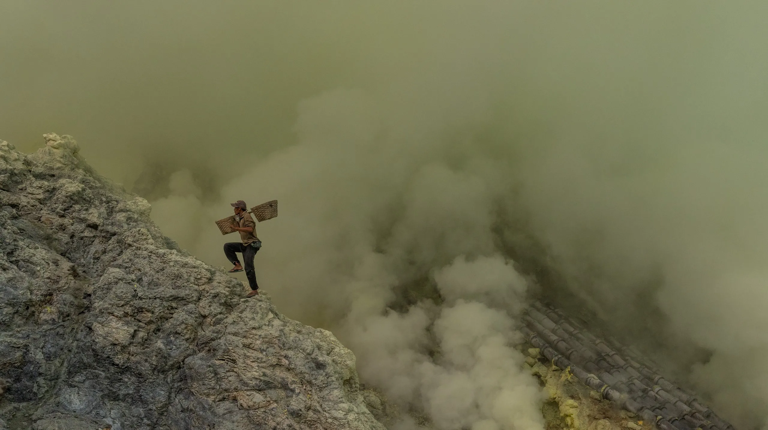 A sulfur carrier on the crater ridge of Kawah Ijen, smoke rising behind him